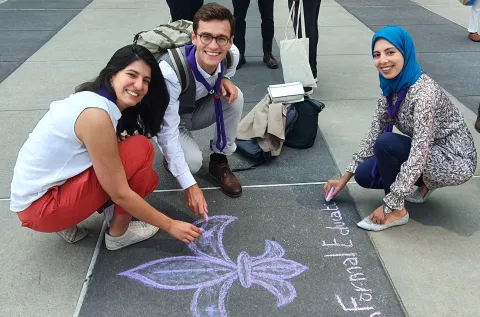 Three Scouts draw the Scout emblem in chalk in front of the United Nations headquarters, and write "non-formal education is also education"