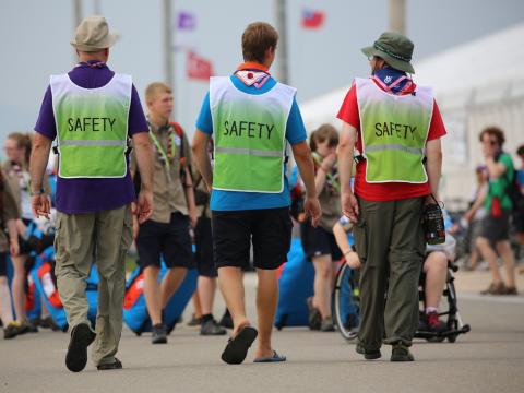 3 responsables scouts avec des gilets de sécurité s'éloignent en direction d'un groupe de Scouts