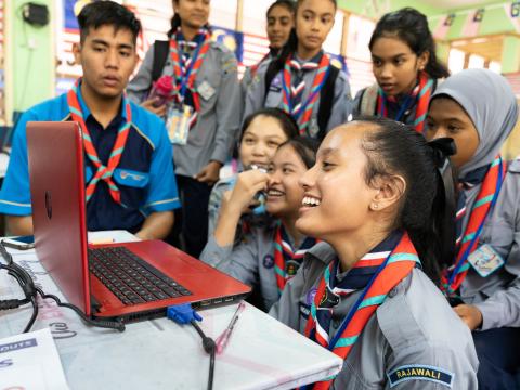 A group of Malaysian Scouts laugh in front of a laptop while they video chat with Scouts in another country