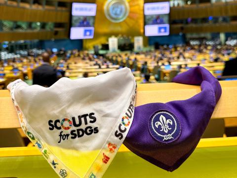 A Scouts for SDGs and World Scouting scarf are displayed on a desk in the foreground of the United Nations General Assembly