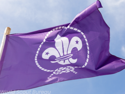 Le drapeau violet de l'OMMS flotte sur fond de ciel bleu.