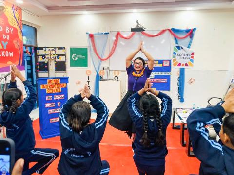 A vibrant yoga session in progress with a World Scouting consultant at the front, and students following along with raised arms in tree pose. They are participating in the movement part of the Mental Health Challenge.