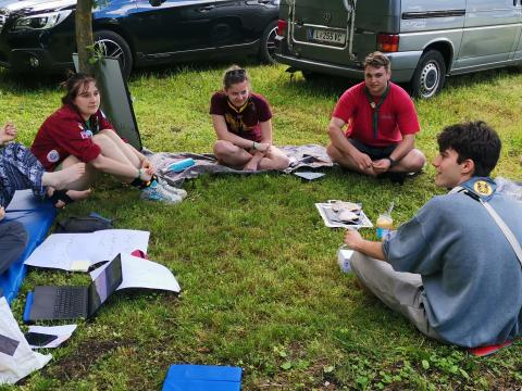 Young people and adults sit on the grass making a circle.
