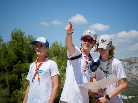 Three Scouts in nature. One of them holds a map and points out.