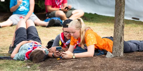 Scouts lay on the ground and take a break from the World Scout Jamboree to check their phones