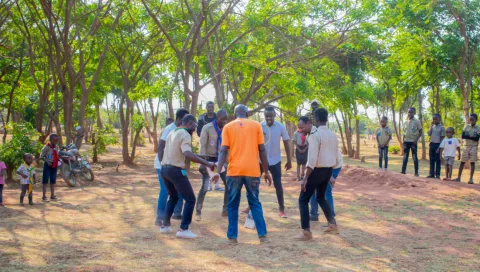 A group of adolescents stand in a circle doing an activity during a Scout event for refugees in Malawi