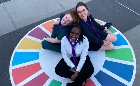 Three World Scouting Youth Representatives, from Kenya, Lithuania and Australia, sit on an SDG wheel at the United Nations HQ in NYC