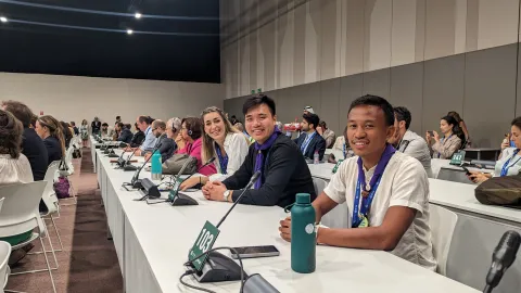 WOSM Youth Representativse Kek, Lucas and Laura sit in a negotiation room at COP28 to listen to a briefing for observers