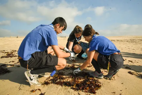 3 young people picking up litter from a beach.